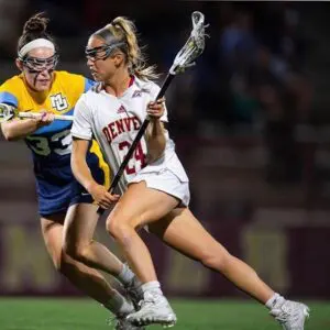 A woman in white shirt and blue shorts playing lacrosse.